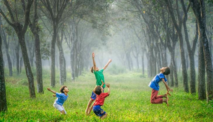 صورة لأربعة أولاد يلعبون بالطابة في غابة خضراء.