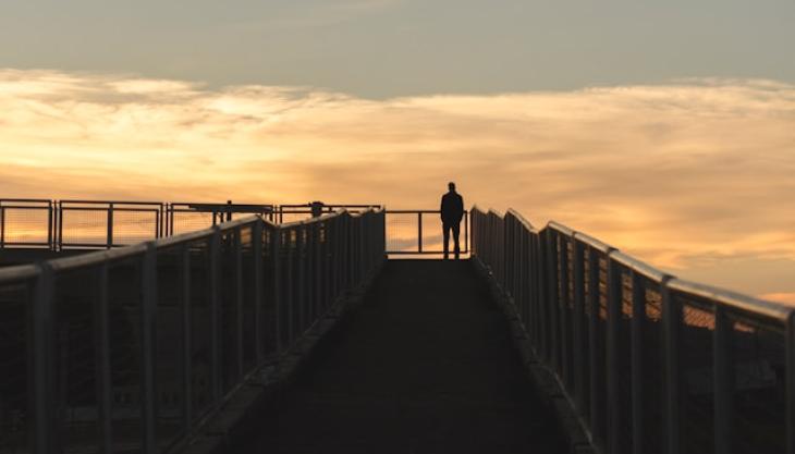 صورة لرجل وحيد واقف على جسر خشبي مقابل المحيط. 