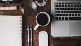 صورة عليا لمكتب وُضع عليه: حاسوب، كوب قهوة، أقلام...